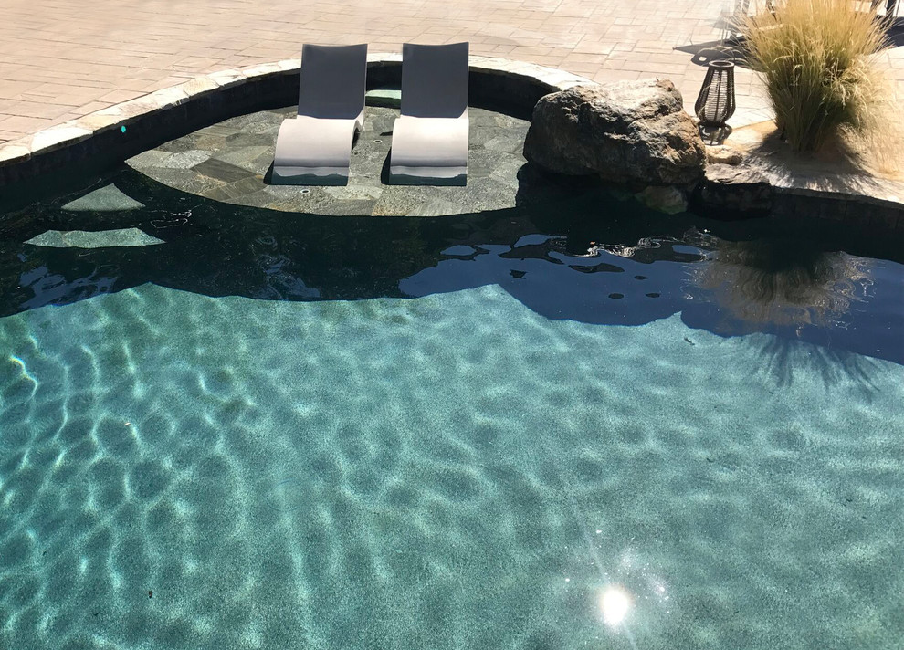 Immagine di una grande piscina naturale moderna personalizzata dietro casa con una vasca idromassaggio e pavimentazioni in pietra naturale