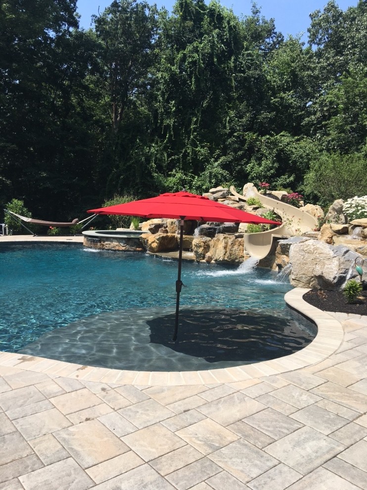 Ejemplo de piscina con tobogán natural clásica grande a medida en patio trasero con adoquines de ladrillo