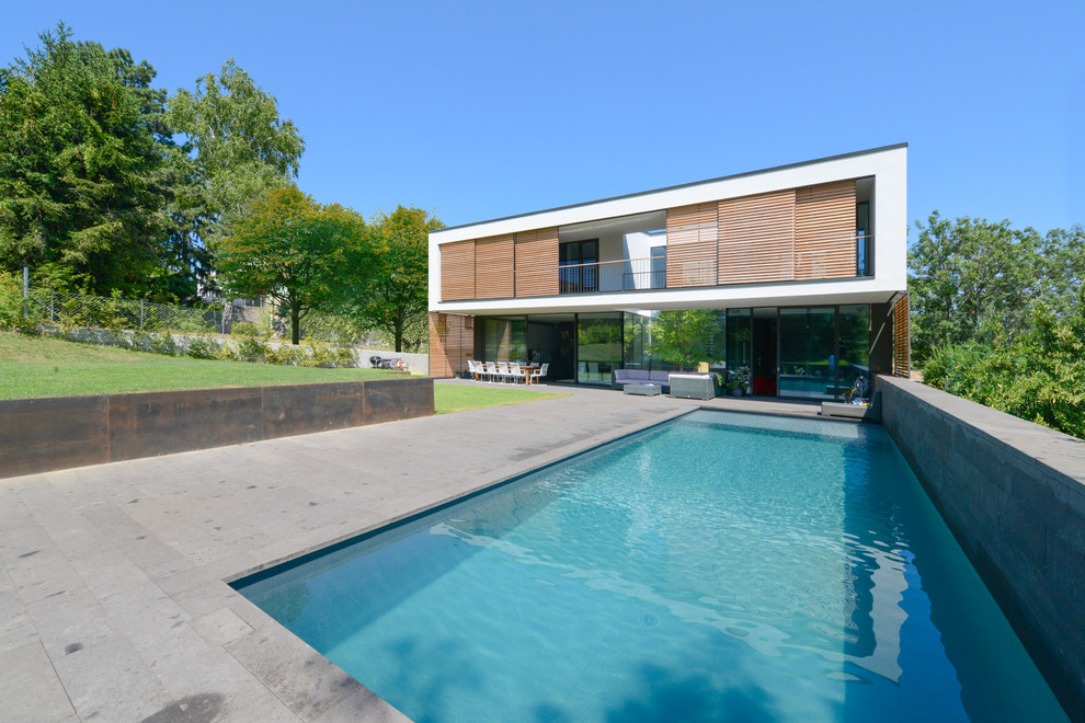 Exempel på en mellanstor modern rektangulär pool på baksidan av huset, med marksten i betong