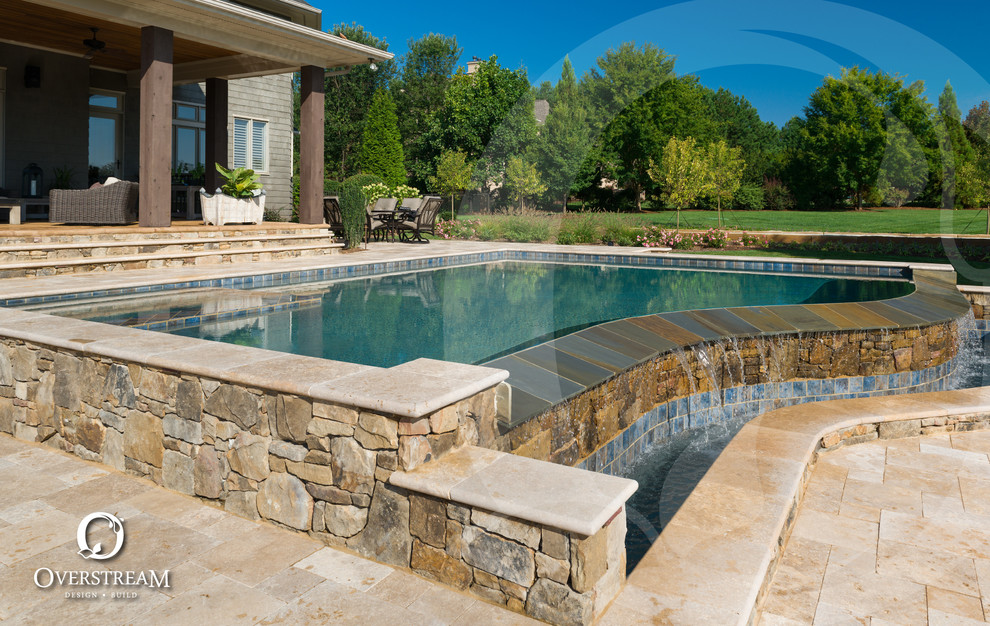 Aménagement d'une grande piscine à débordement et arrière moderne sur mesure avec un bain bouillonnant et des pavés en pierre naturelle.