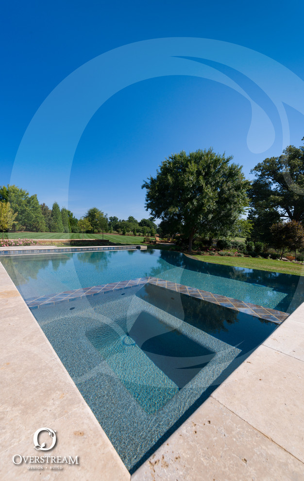 Idée de décoration pour une grande piscine à débordement et arrière minimaliste sur mesure avec un bain bouillonnant et des pavés en pierre naturelle.