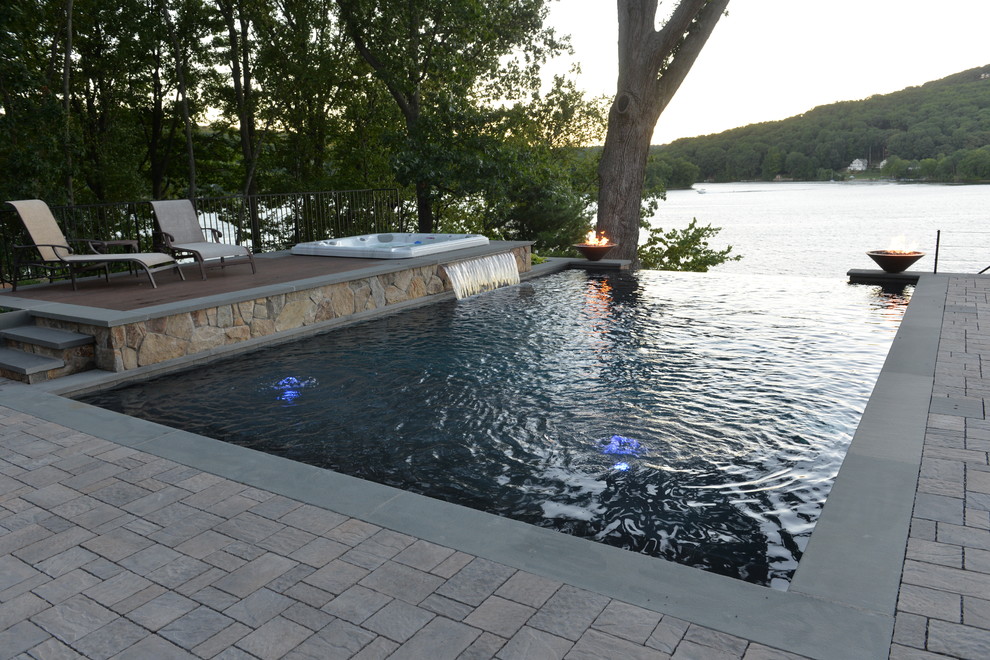 This is an example of a medium sized contemporary back rectangular infinity swimming pool in New York with a water feature and natural stone paving.