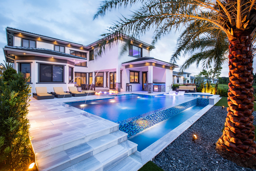 Immagine di una grande piscina a sfioro infinito minimalista personalizzata dietro casa con paesaggistica bordo piscina e pavimentazioni in pietra naturale