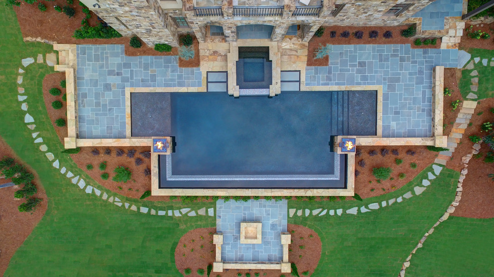 Imagen de piscina con fuente infinita tradicional grande a medida en patio trasero con adoquines de piedra natural