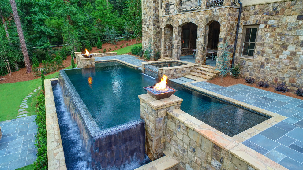 Diseño de piscina con fuente infinita clásica grande a medida en patio trasero con adoquines de piedra natural