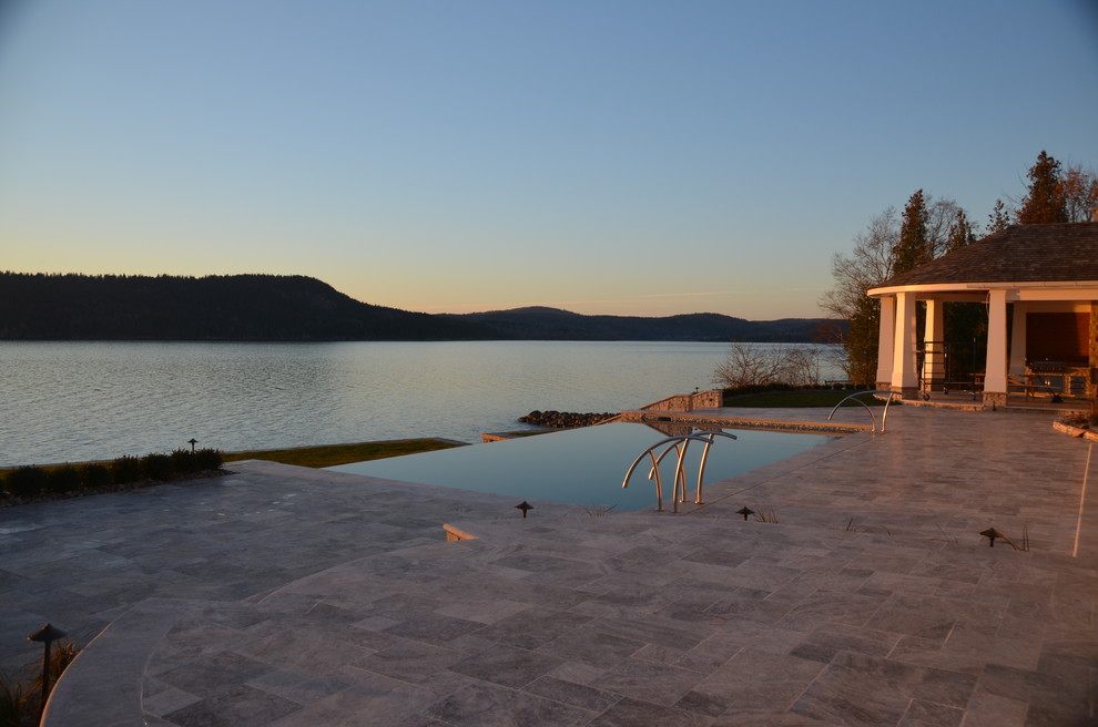 Example of a large trendy backyard stone and rectangular infinity pool design in Other