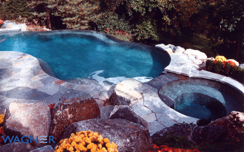 Cette image montre une grande piscine à débordement et arrière traditionnelle sur mesure avec un point d'eau et des pavés en pierre naturelle.