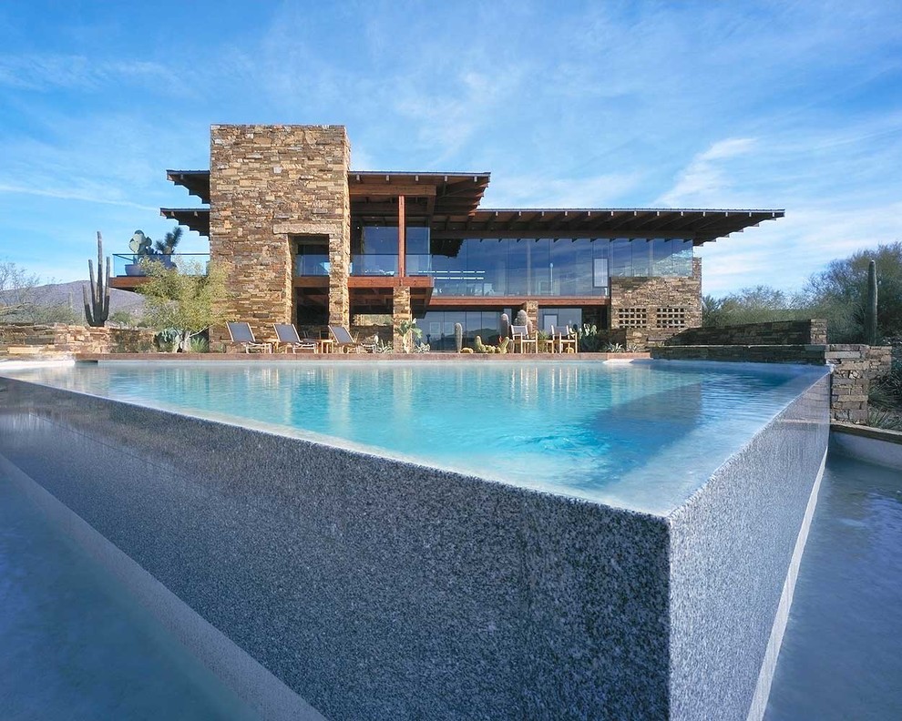 Modelo de piscina infinita moderna grande a medida en patio trasero con suelo de hormigón estampado