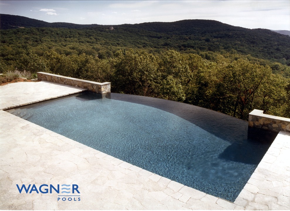 Large traditional back rectangular infinity swimming pool in New York with a water feature and natural stone paving.