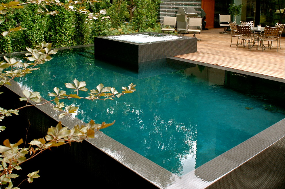 Example of a large minimalist backyard rectangular infinity hot tub design in Other with decking