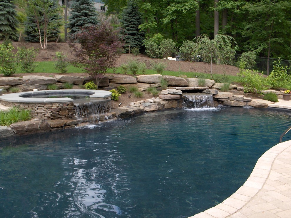 Cette image montre une grande piscine naturelle et avant chalet sur mesure avec des pavés en béton et un bain bouillonnant.