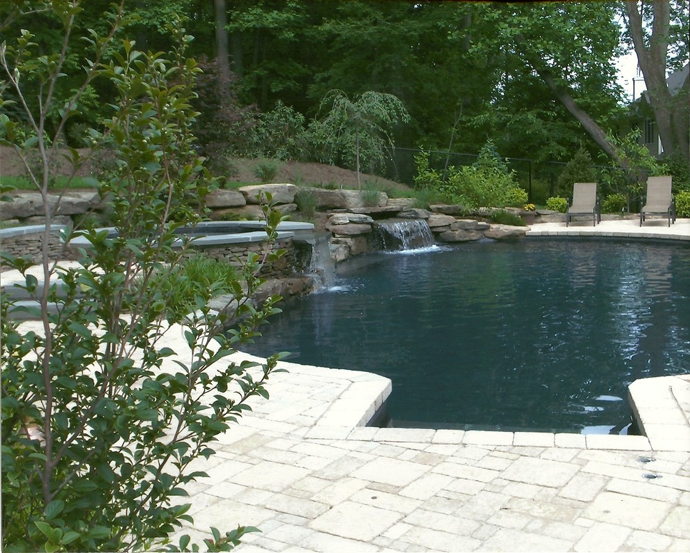 Réalisation d'une grande piscine naturelle et arrière chalet sur mesure avec des pavés en béton et un bain bouillonnant.