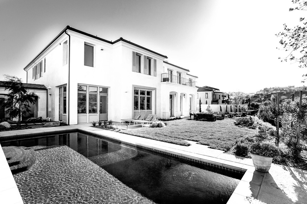 Modelo de casa de la piscina y piscina natural clásica de tamaño medio rectangular en patio trasero con adoquines de hormigón