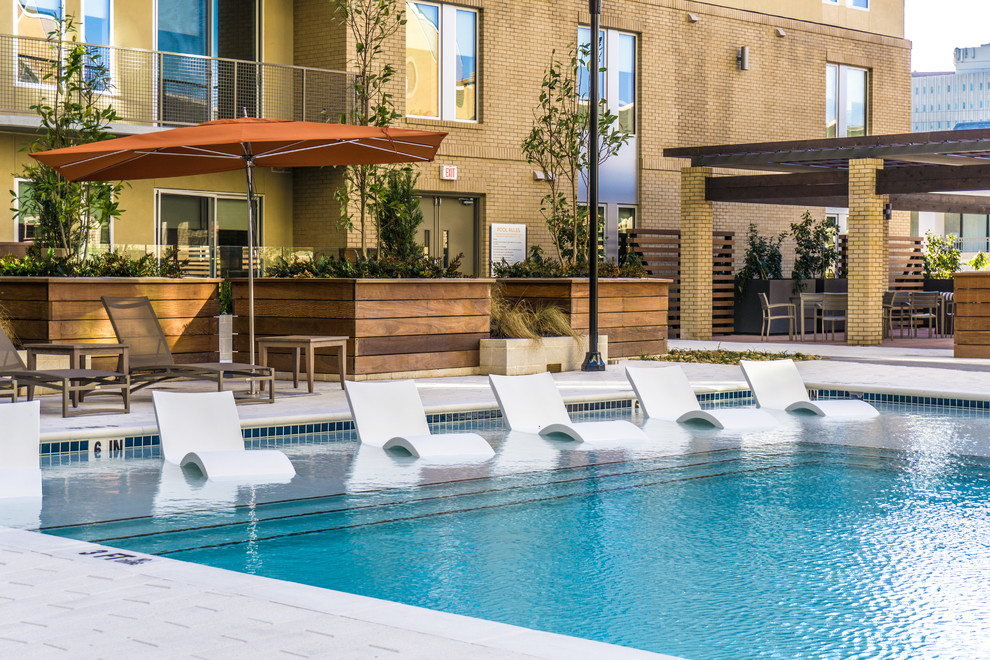 Diseño de piscina con fuente minimalista extra grande en forma de L en patio con adoquines de hormigón