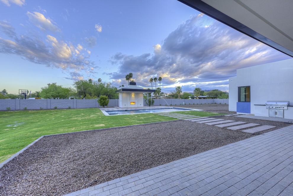 Ejemplo de piscina con fuente alargada minimalista de tamaño medio rectangular en patio trasero con adoquines de hormigón
