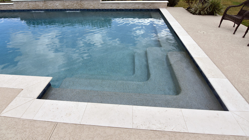Réalisation d'une grande piscine arrière minimaliste rectangle avec une terrasse en bois.