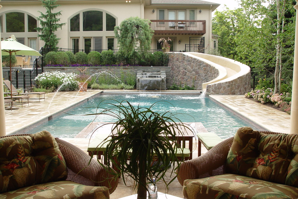 Diseño de piscina con tobogán mediterránea grande rectangular en patio trasero con adoquines de piedra natural