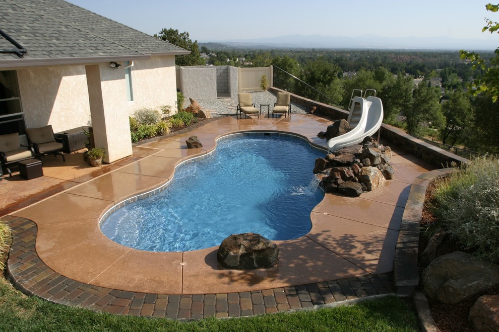 Diseño de piscina con tobogán marinera de tamaño medio a medida en patio trasero con adoquines de piedra natural