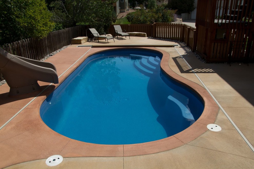 Diseño de piscina con tobogán de estilo americano pequeña tipo riñón en patio trasero con losas de hormigón