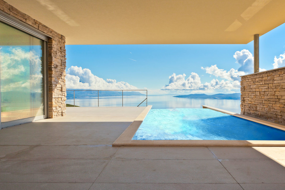 Mittelgroßer Moderner Infinity-Pool hinter dem Haus in rechteckiger Form mit Natursteinplatten in Sonstige