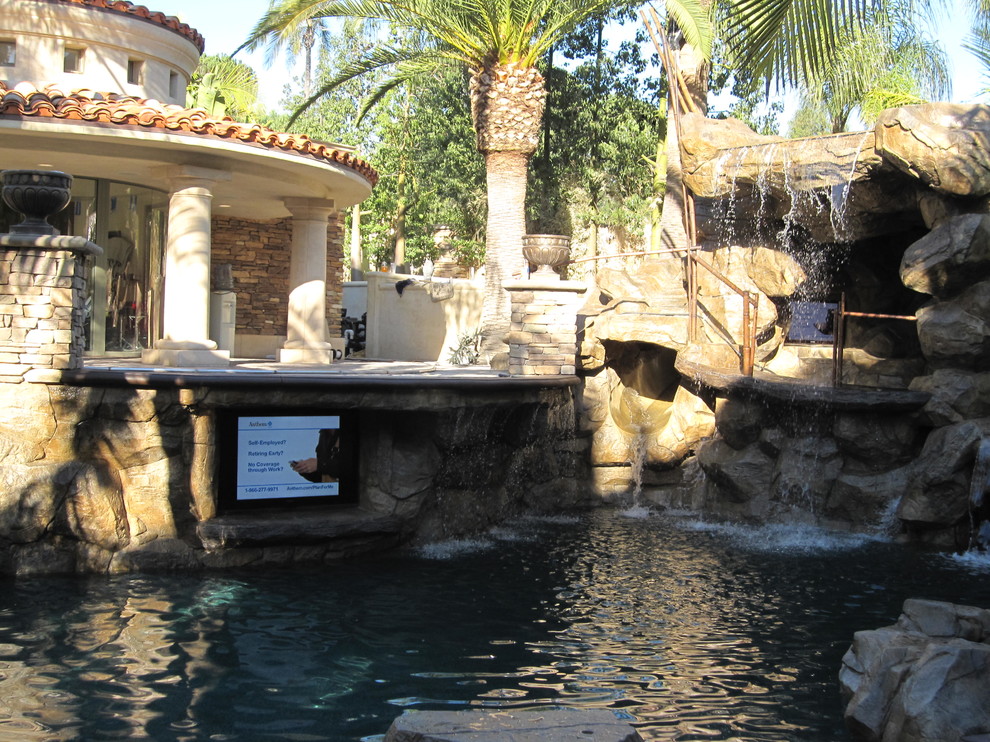 Foto di una grande piscina fuori terra tropicale personalizzata dietro casa con fontane e pavimentazioni in pietra naturale