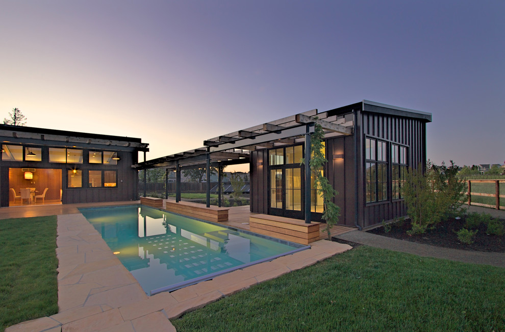 Modern inredning av en stor rektangulär infinitypool på baksidan av huset, med poolhus och naturstensplattor
