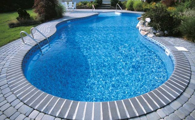 Ejemplo de piscina alargada tradicional de tamaño medio a medida en patio trasero con adoquines de ladrillo