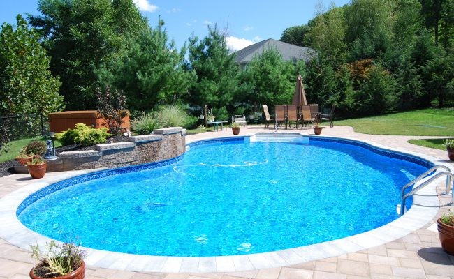 Modelo de piscina con fuente alargada tradicional de tamaño medio a medida en patio trasero con adoquines de ladrillo