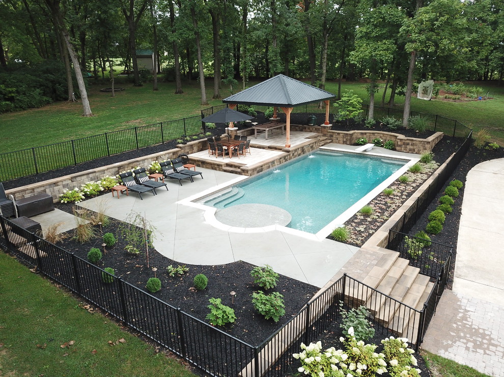 Foto de piscina con fuente natural actual grande rectangular en patio trasero con suelo de hormigón estampado