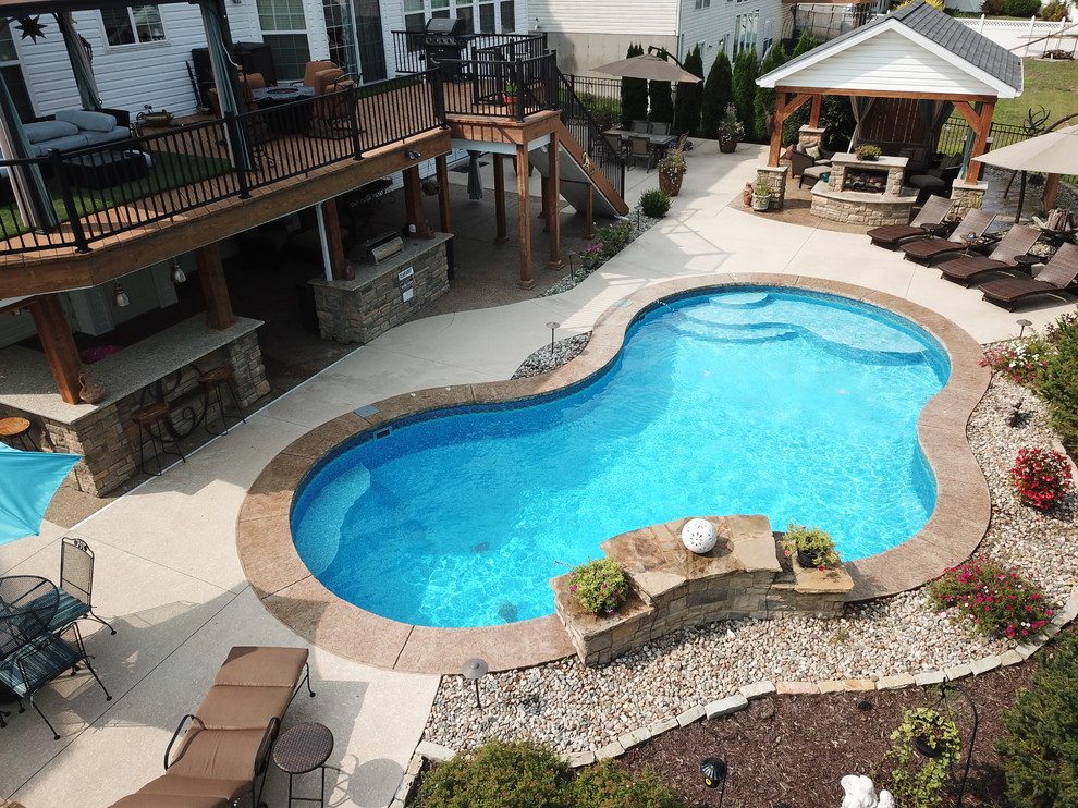Diseño de piscina con fuente actual de tamaño medio a medida en patio trasero con suelo de hormigón estampado