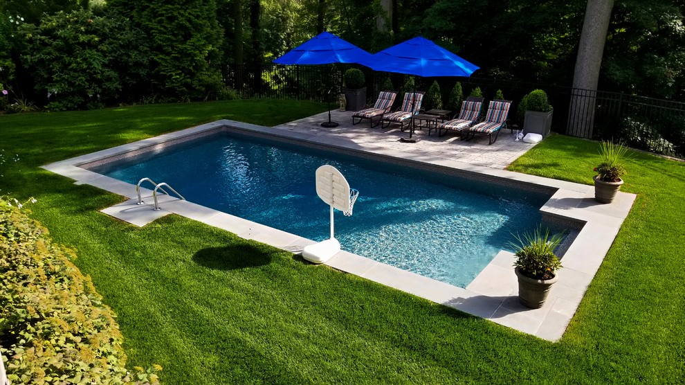 Modelo de piscina alargada clásica de tamaño medio rectangular en patio trasero con adoquines de hormigón