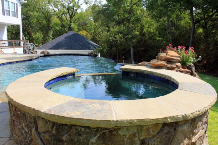 Medium sized contemporary back custom shaped infinity swimming pool in Austin with a water feature and natural stone paving.