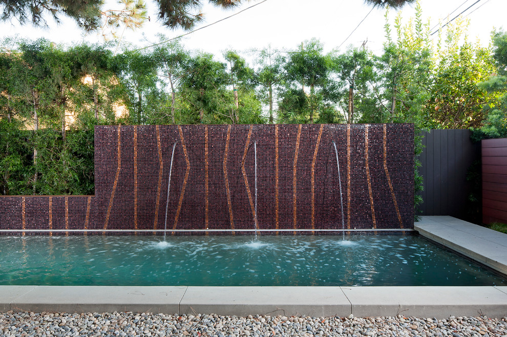 Foto de piscina alargada actual de tamaño medio rectangular en patio trasero con adoquines de hormigón