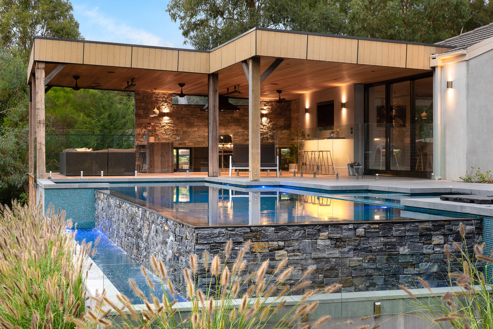 Immagine di una piscina a sfioro infinito design personalizzata dietro casa con una vasca idromassaggio e lastre di cemento