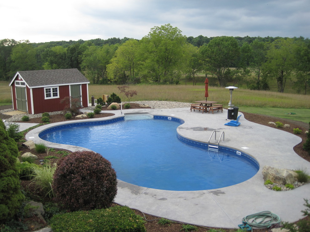 На фото: большой бассейн произвольной формы на заднем дворе в классическом стиле с покрытием из бетонных плит