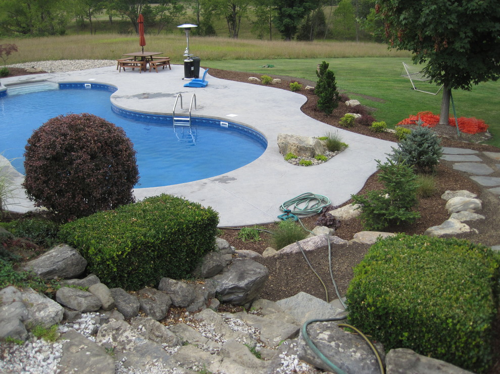 Imagen de piscina clásica grande a medida en patio trasero con losas de hormigón