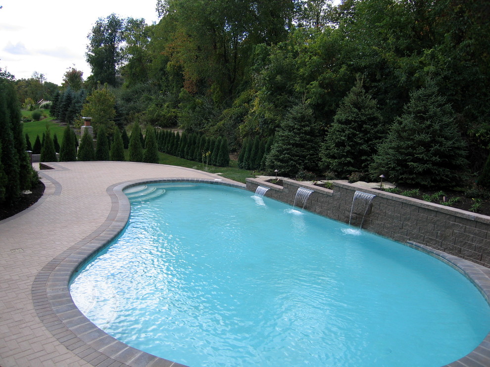 Idee per una grande piscina a "C" dietro casa con fontane e pavimentazioni in mattoni