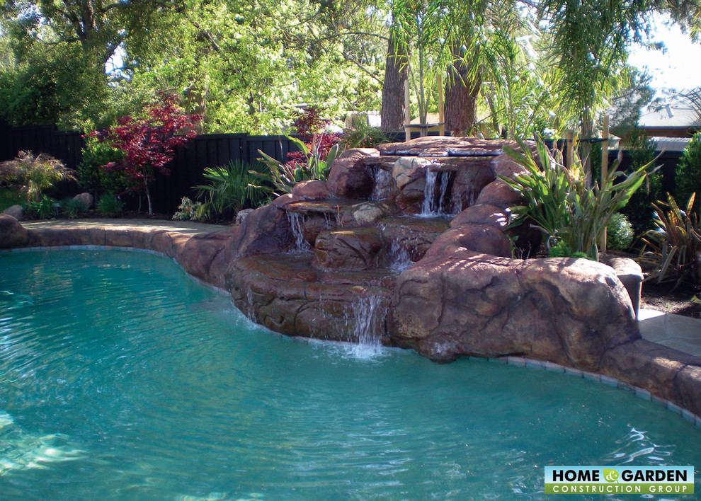 Diseño de piscina natural tropical a medida en patio trasero con adoquines de ladrillo