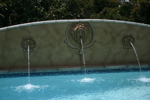 Ejemplo de piscina con fuente elevada ecléctica de tamaño medio rectangular en patio trasero con adoquines de hormigón