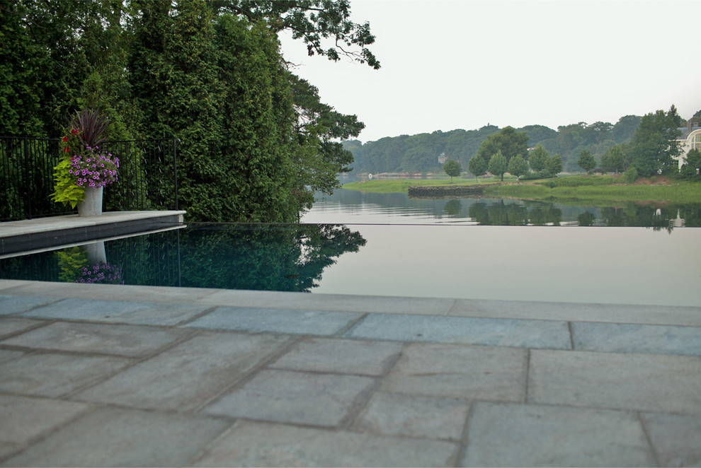Réalisation d'une piscine à débordement et arrière tradition rectangle avec des pavés en pierre naturelle.