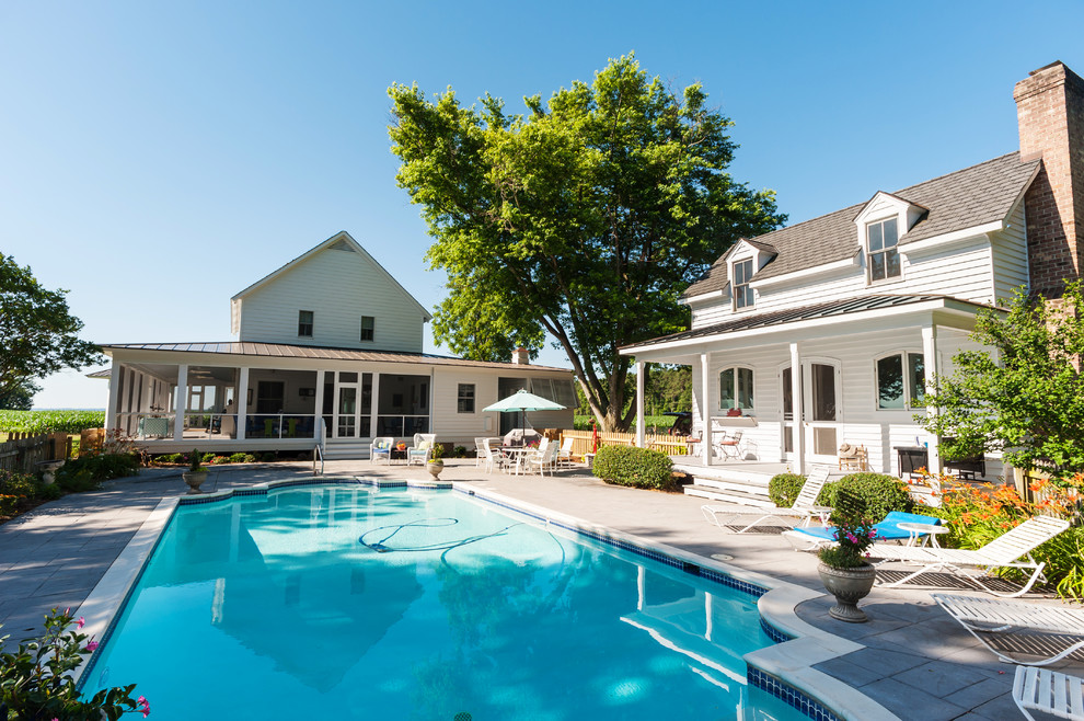 Modelo de casa de la piscina y piscina de estilo de casa de campo de tamaño medio rectangular en patio lateral con suelo de hormigón estampado