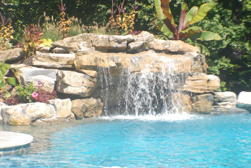 Foto di una grande piscina a sfioro infinito tropicale personalizzata dietro casa con fontane e pavimentazioni in pietra naturale