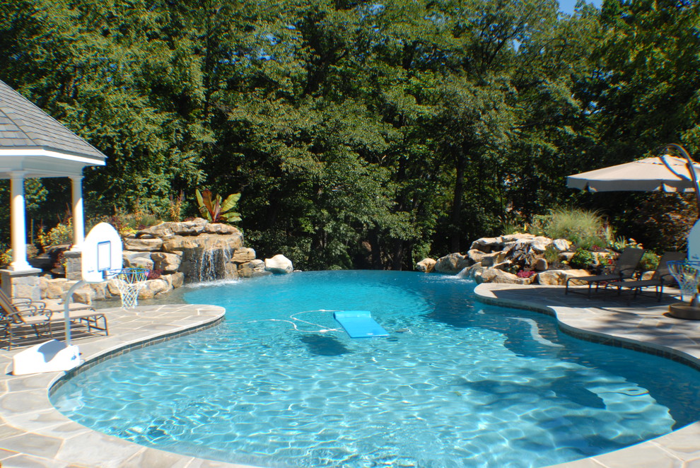 Imagen de piscina con fuente infinita exótica grande a medida en patio trasero con adoquines de piedra natural