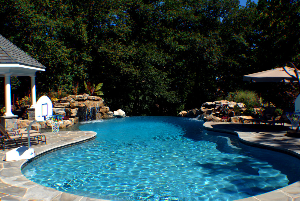 Cette photo montre une grande piscine à débordement et arrière exotique sur mesure avec un point d'eau et des pavés en pierre naturelle.