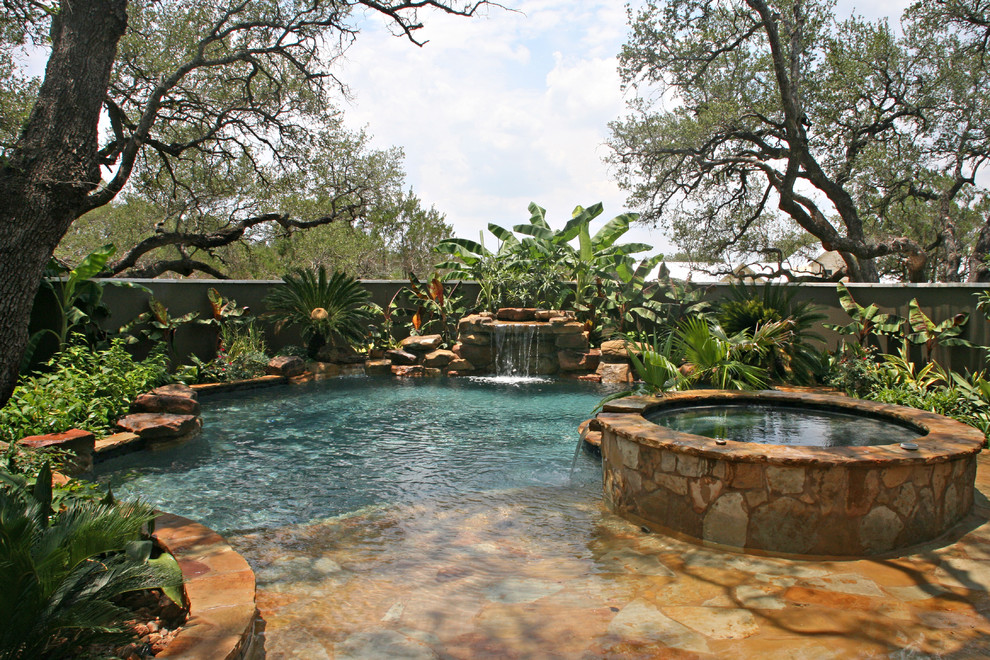 Esempio di una piscina naturale tropicale personalizzata di medie dimensioni e dietro casa con pavimentazioni in pietra naturale e una vasca idromassaggio