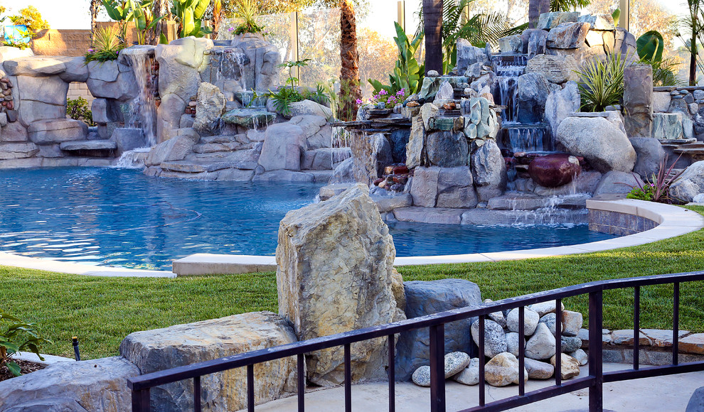 Aménagement d'une grande piscine arrière et naturelle exotique sur mesure avec un bain bouillonnant et des pavés en pierre naturelle.