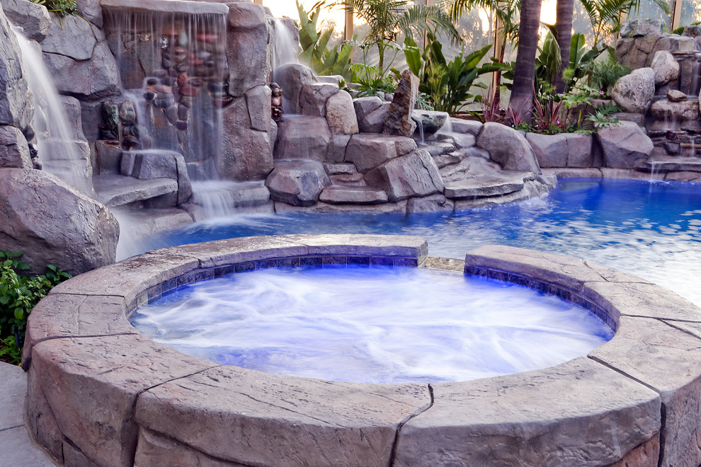 Diseño de piscinas y jacuzzis naturales tropicales grandes a medida en patio trasero con adoquines de piedra natural