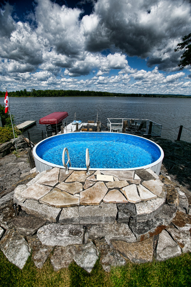 Imagen de piscina elevada rústica pequeña redondeada con adoquines de piedra natural