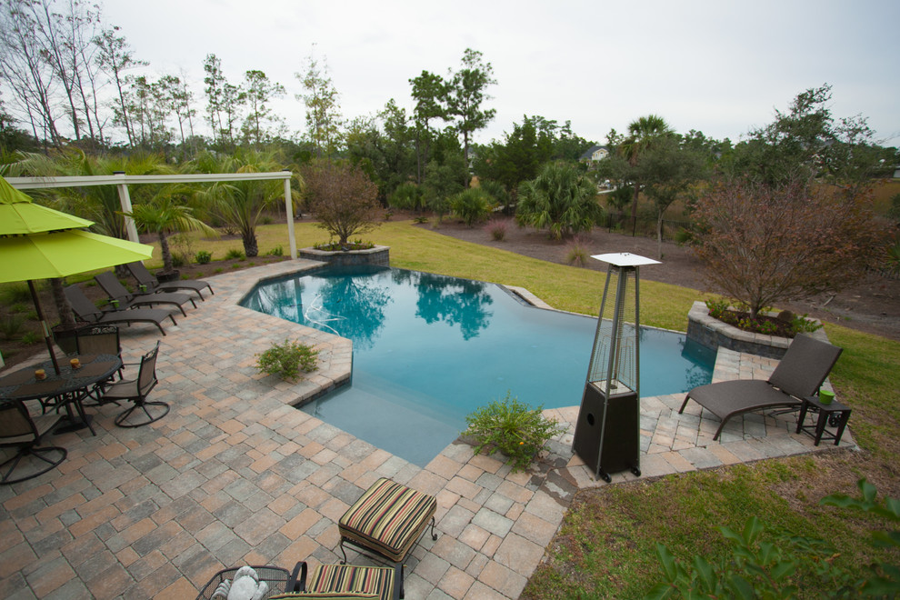 Ejemplo de piscina con fuente infinita tradicional grande a medida en patio trasero con adoquines de ladrillo