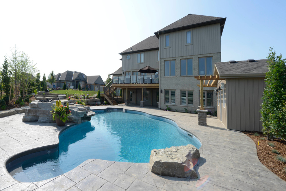 This is an example of a back custom shaped swimming pool in Toronto with a pool house and stamped concrete.